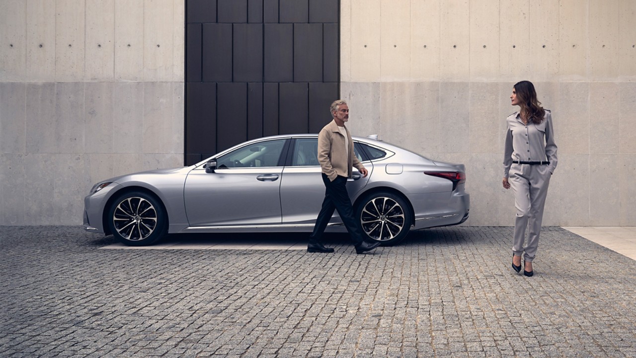 A man and woman stood next to a parked Lexus LS